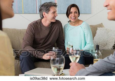 Stock Image - Mature friends socialising with white wine. Fotosearch