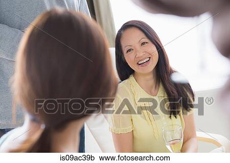 Stock Image - Mature friends socialising with white wine. Fotosearch