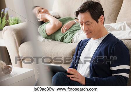 Mature man using digital tablet, woman lying on sofa View Large Photo Image Stock Photo - Mature man using digital tablet, woman lying on sofa. Fotosearch