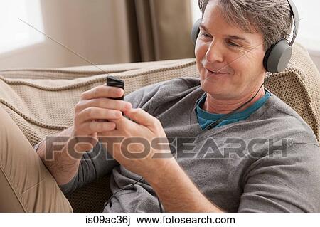 Stock Image - Mature man wearing headphones using cell phone. Fotosearch