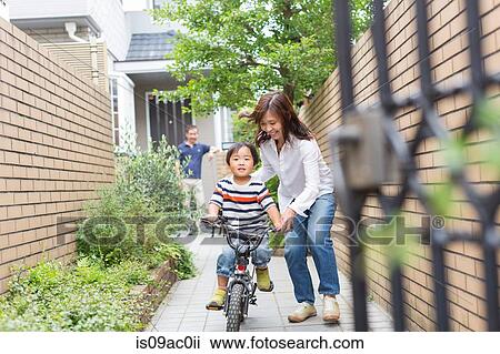 Stock Image - Mother helping son to ride a bike. Fotosearch