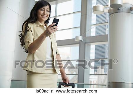 Stock Image - Portrait of woman in Staten Island Ferry terminal with smartphone and wheeled suitcase. Fotosearch