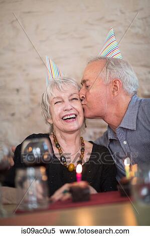 Stock Photography - Senior couple wearing party hats, man kissing woman on cheek. Fotosearch