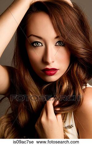 Stock Image - Studio portrait of brunette woman with hands in hair. Fotosearch