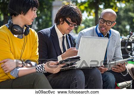Stock Image - Three casual businesspeople using laptop in park. Fotosearch