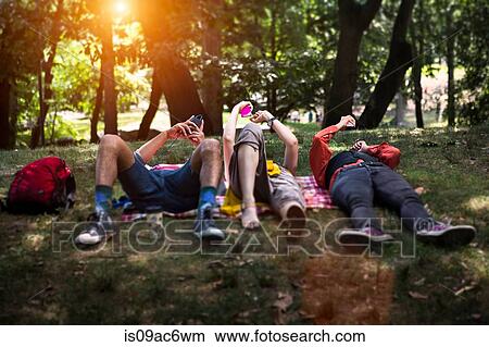 Picture - Three friends lying on picnic blanket in park. Fotosearch