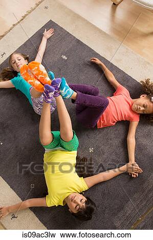Stock Photo - Three girls lying on floor with legs raised. Fotosearch