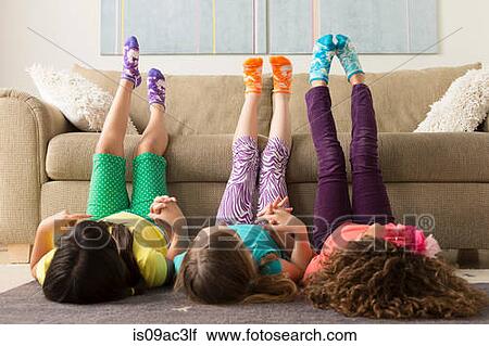 Stock Image - Three girls lying on floor with legs up. Fotosearch