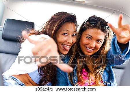 Stock Photography - Two female friends making hand gestures in car. Fotosearch