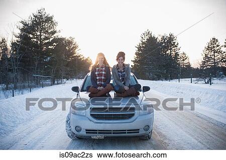 Two women sitting on car bonnet in snow View Large Photo Image Stock Photograph - Two women sitting on car bonnet in snow. Fotosearch