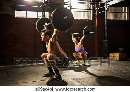 Two young adults lifting barbells in gym View Large Photo Image Stock Image - Two young adults lifting barbells in gym. Fotosearch