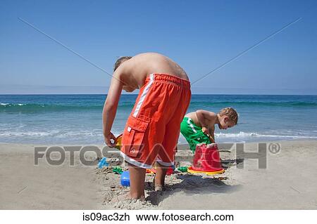 Two young brothers building sandcastles on beach View Large Photo Image Stock Image - Two young brothers building sandcastles on beach. Fotosearch