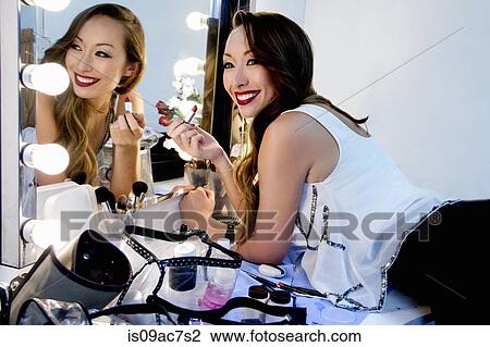 Stock Image - Woman applying lipstick in mirror. Fotosearch
