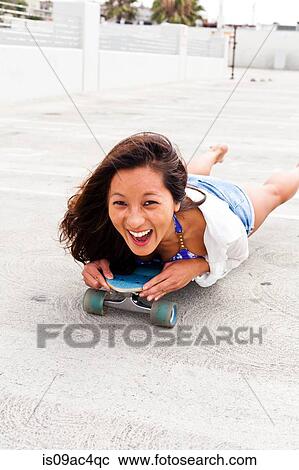 Stock Image - Woman in parking lot lying on skateboard. Fotosearch