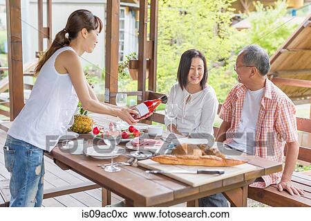 Stock Image - Woman serving wine to parents at dining table. Fotosearch