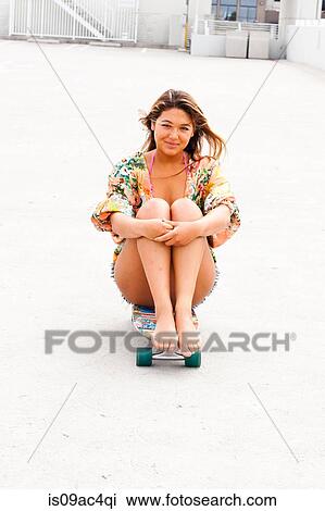 Stock Image - Woman sitting on skateboard, Hermosa Beach, California, USA. Fotosearch