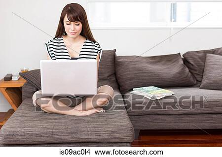 Picture - Woman sitting on sofa using laptop. Fotosearch