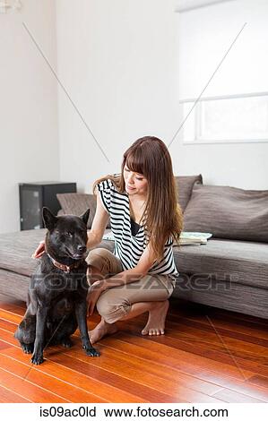 Stock Image - Woman with dog in living room. Fotosearch