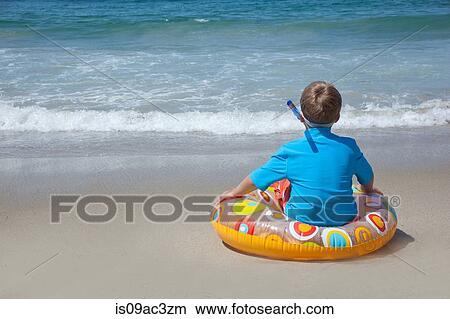 Picture - Young boy sitting on rubber ring on beach. Fotosearch