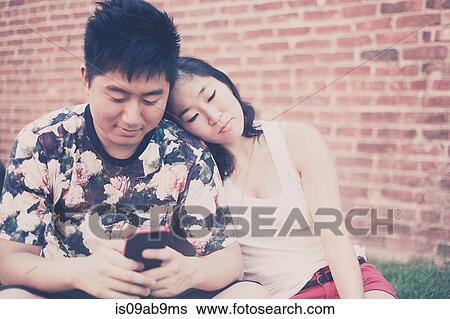 Stock Photograph - Young couple sitting down in front of brick wall. Fotosearch
