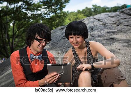 Young couple wearing earphones using tablet View Large Photo Image Stock Image - Young couple wearing earphones using tablet. Fotosearch