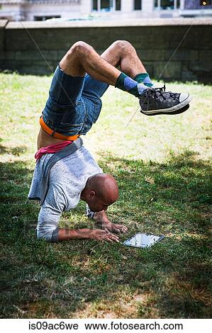 Stock Image - Young man doing handstand using tablet. Fotosearch