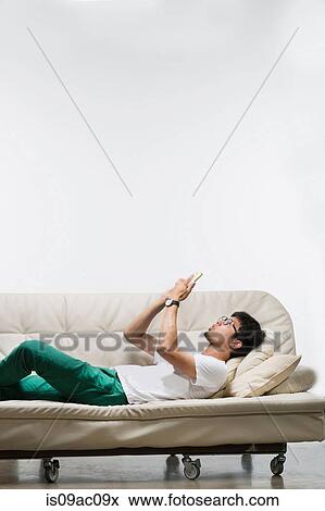 Stock Photo - Young man lying on sofa using smartphone. Fotosearch