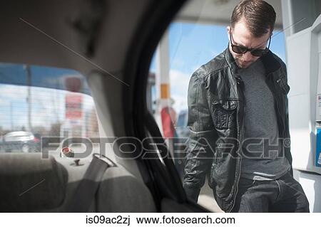 Stock Image - Young man putting fuel in car, view from vehicle interior. Fotosearch