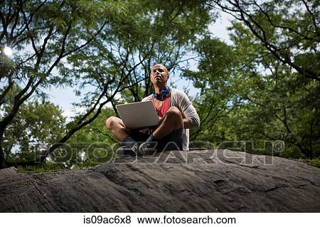 Young man sitting on rocks using laptop View Large Photo Image Stock Photo - Young man sitting on rocks using laptop. Fotosearch