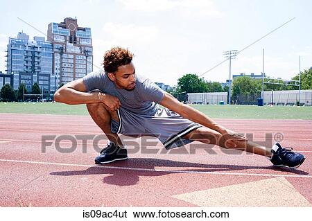 Stock Photograph - Young man stretching leg on running track. Fotosearch