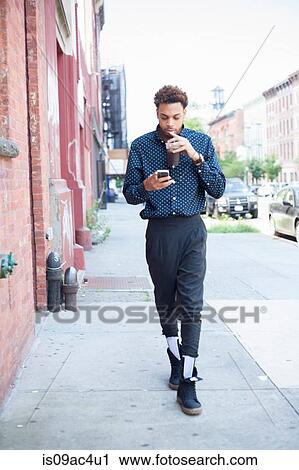 Young man walking down street with cellphone and drink View Large Photo Image Stock Image - Young man walking down street with cellphone and drink. Fotosearch