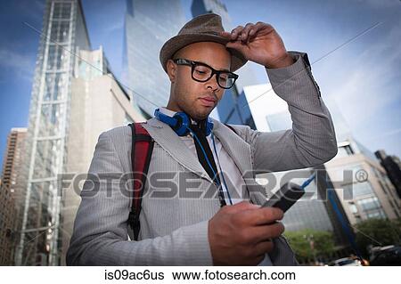 Stock Photograph - Young man wearing hat and glasses using mp3 player. Fotosearch