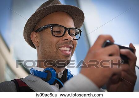 Young man wearing hat and glasses using mp3 player View Large Photo Image Stock Photograph - Young man wearing hat and glasses using mp3 player. Fotosearch