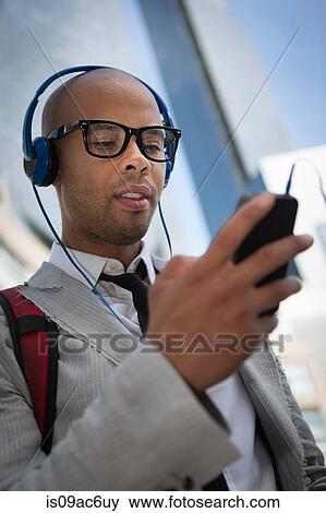 Stock Photo - Young man wearing headphones and glasses using mp3 player. Fotosearch
