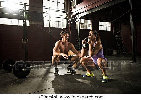 Stock Image - Young woman and personal trainer working out in gym. Fotosearch