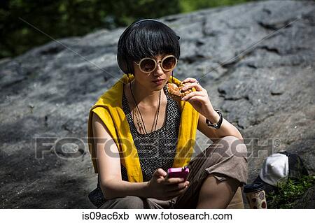 Stock Image - Young woman eating snack with mp3 player. Fotosearch