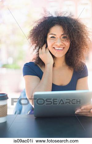 Stock Image - Young woman holding digital tablet at sidewalk cafe. Fotosearch