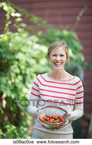 Stock Image - Young woman holding sieve with tomatoes. Fotosearch
