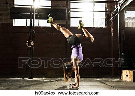 Stock Photo - Young woman in gym doing handstand. Fotosearch