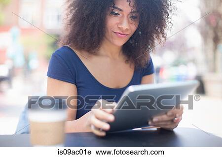 Stock Image - Young woman looking at digital tablet at sidewalk cafe. Fotosearch