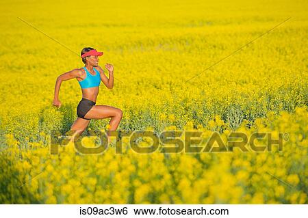 Stock Photograph - Young woman running in oil seed rape field. Fotosearch