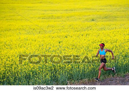 Stock Image - Young woman running next to oil seed rape field. Fotosearch
