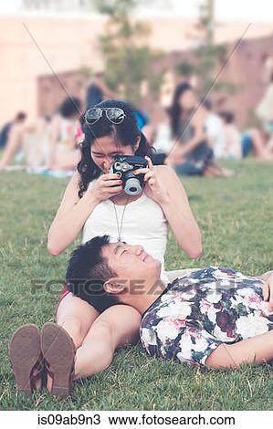Stock Image - Young woman taking photograph of boyfriend. Fotosearch