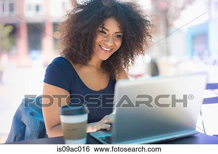 Stock Photograph - Young woman using laptop at sidewalk cafe. Fotosearch
