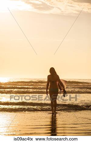 Stock Photo - Young woman with surfboard at sunset, La Jolla, San Diego, California, USA. Fotosearch