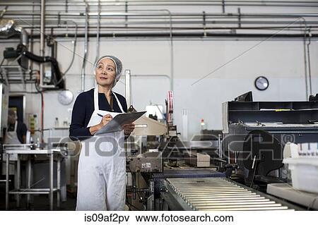 Stock Photo - Factory worker making notes on clipboard by production line. Fotosearch