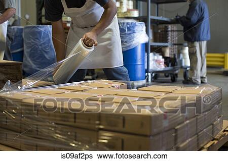 Stock Photograph - Factory worker wrapping cardboard boxes with clingfilm. Fotosearch