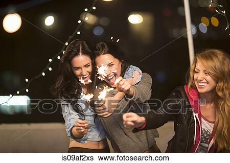 Stock Photograph - Female friends with sparklers at rooftop party. Fotosearch