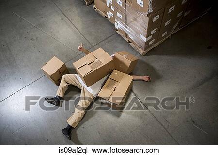Stock Image - Man lying on floor covered by cardboard boxes in warehouse. Fotosearch