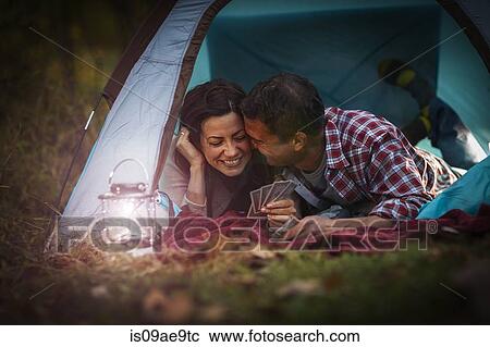 Stock Image - Mature couple lying together in tent, playing card game. Fotosearch
